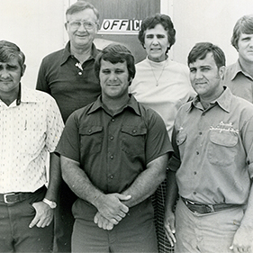 A black and white photo of Devall Towing's founders standing outside of their office for a group photo