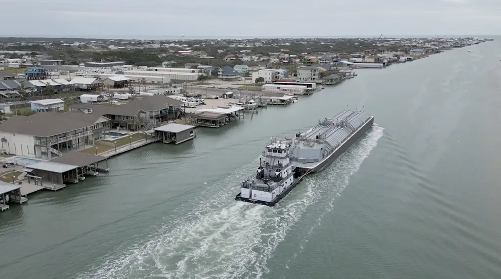 A Southern Devall barge transporting fertilizing while passing by a series of bay houses