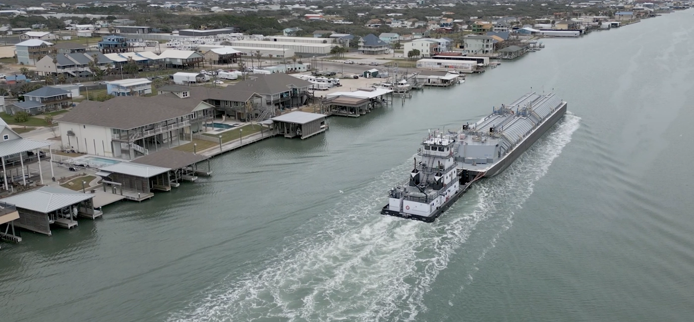 A Southern Devall barge transporting fertilizing while passing by a series of bay houses