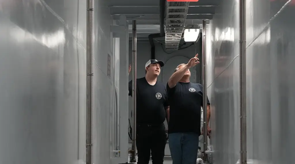 Two Southern Devall employees in black shirts checking on pipes inside a barge