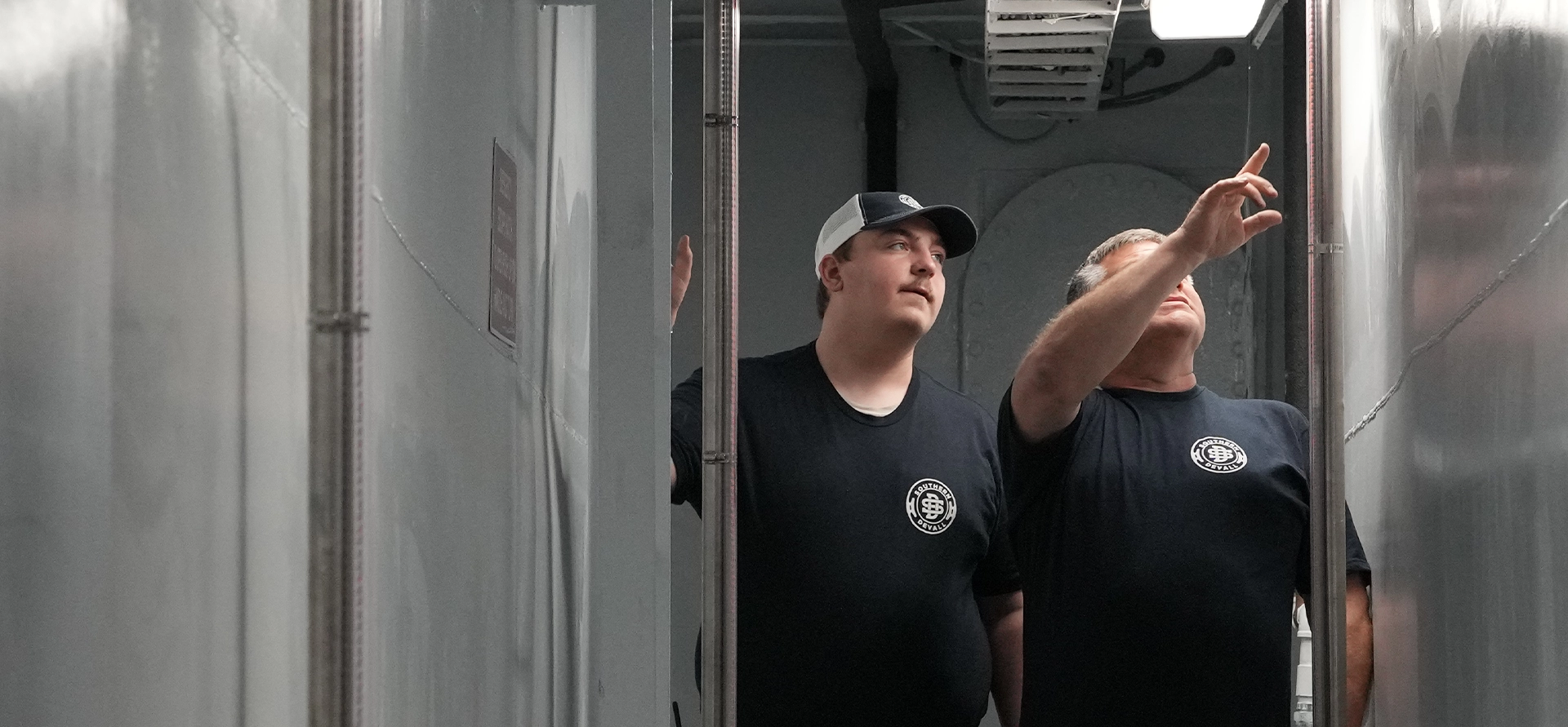 Two Southern Devall employees in black shirts checking on pipes inside a barge