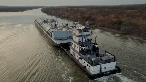 A Southern Devall towboat moving an fertilizer barge up a river in the late afternoon